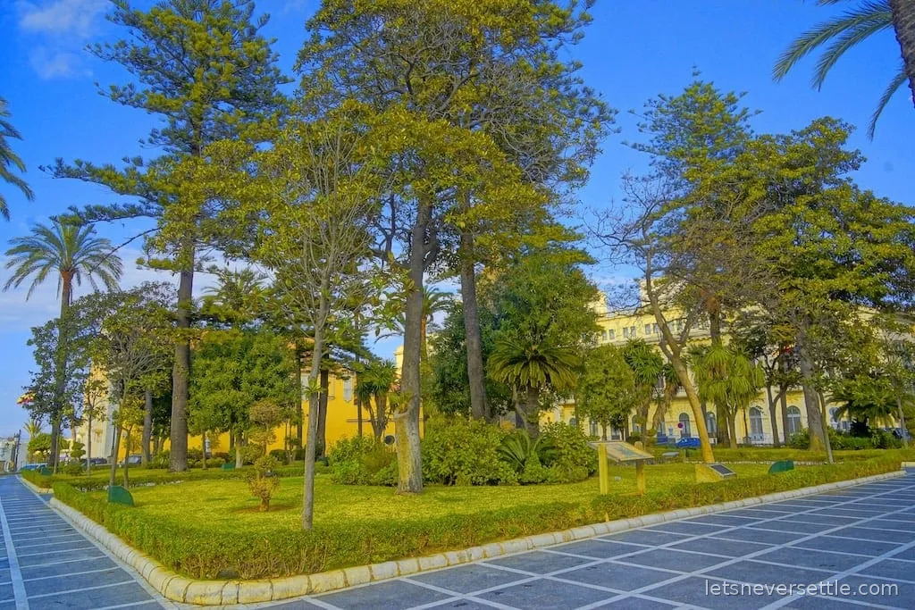 Manicured gardens with palms and araucaria trees in front of grand yellow buildings