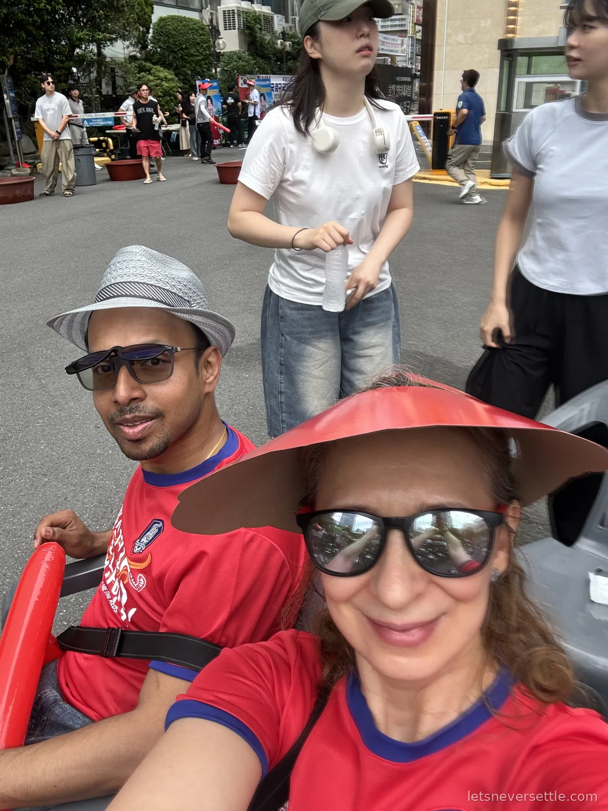 Selfie of Inga and Dileep in red Korea national team shirts on a Changwon street, other fans walking past behind them