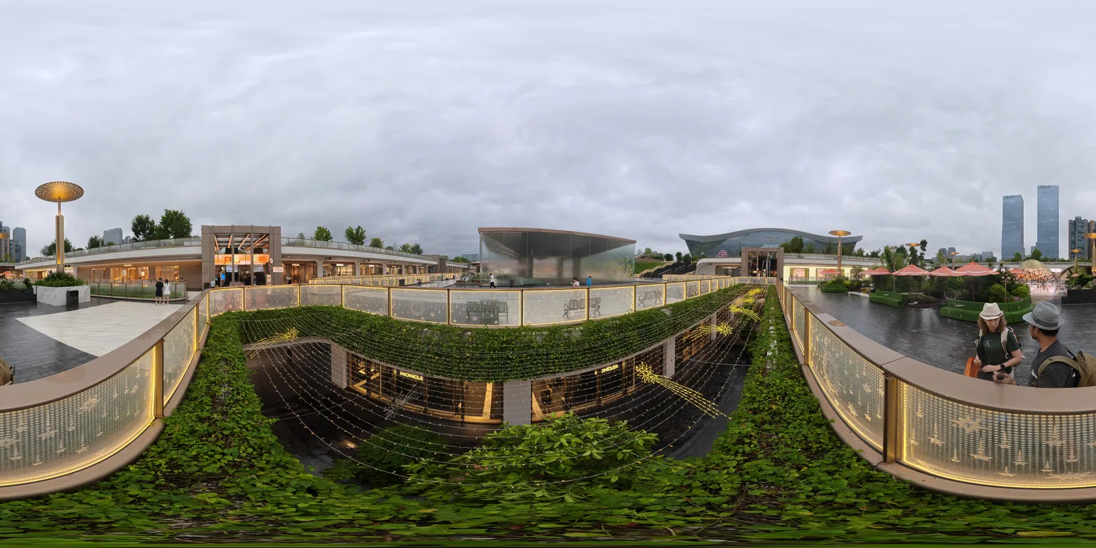 The planted rooftop park at SKP Chengdu, terraces of greenery and a glass balustrade strung with lights, a sunken courtyard of shopfronts below and city towers on the skyline