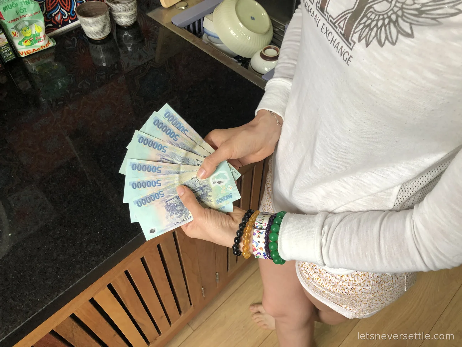 Inga's hands fanning out seven 500,000 Vietnamese dong notes over a dark granite kitchen counter