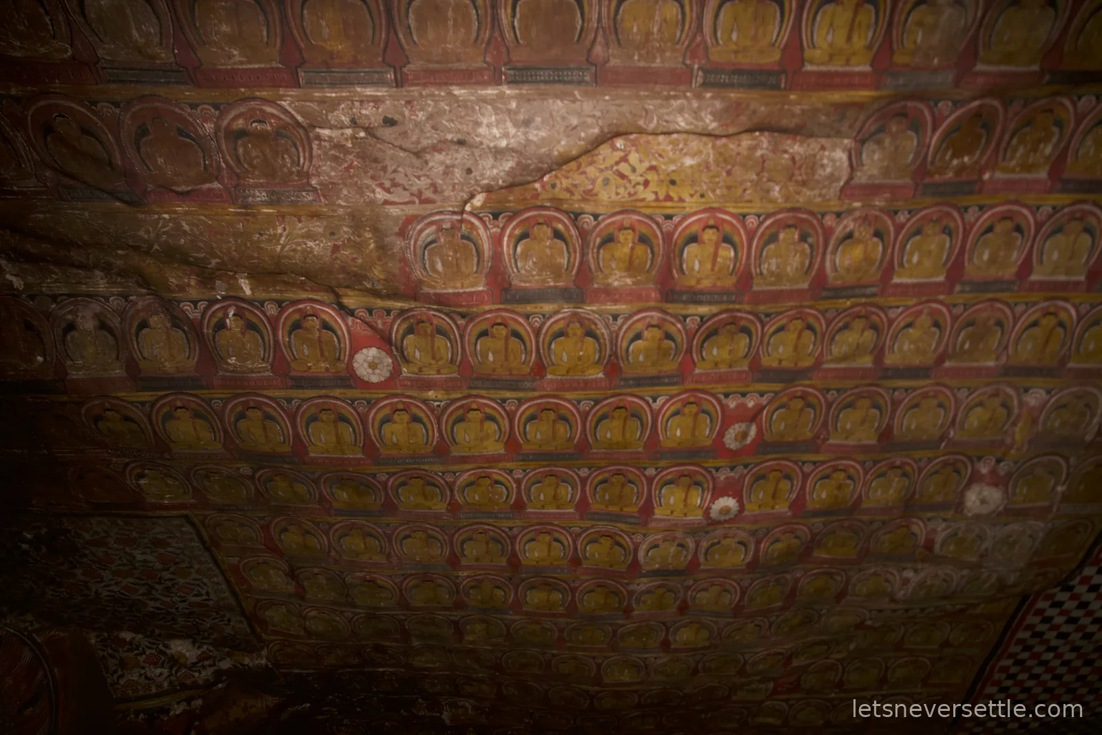 Cave ceiling at Dambulla painted edge to edge with rows of repeated seated Buddha figures in red and gold