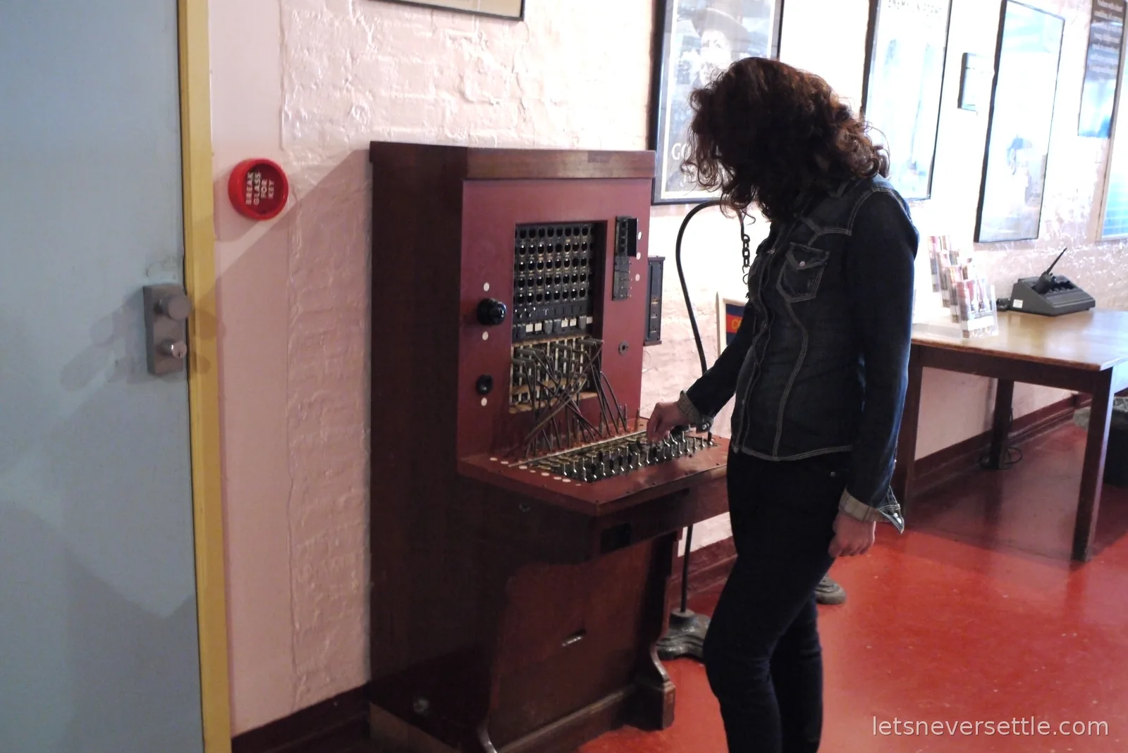 Inga plugging a cable into a vintage wooden telephone switchboard in the wartime tunnels exhibition at Dover Castle, framed wartime posters on the wall behind