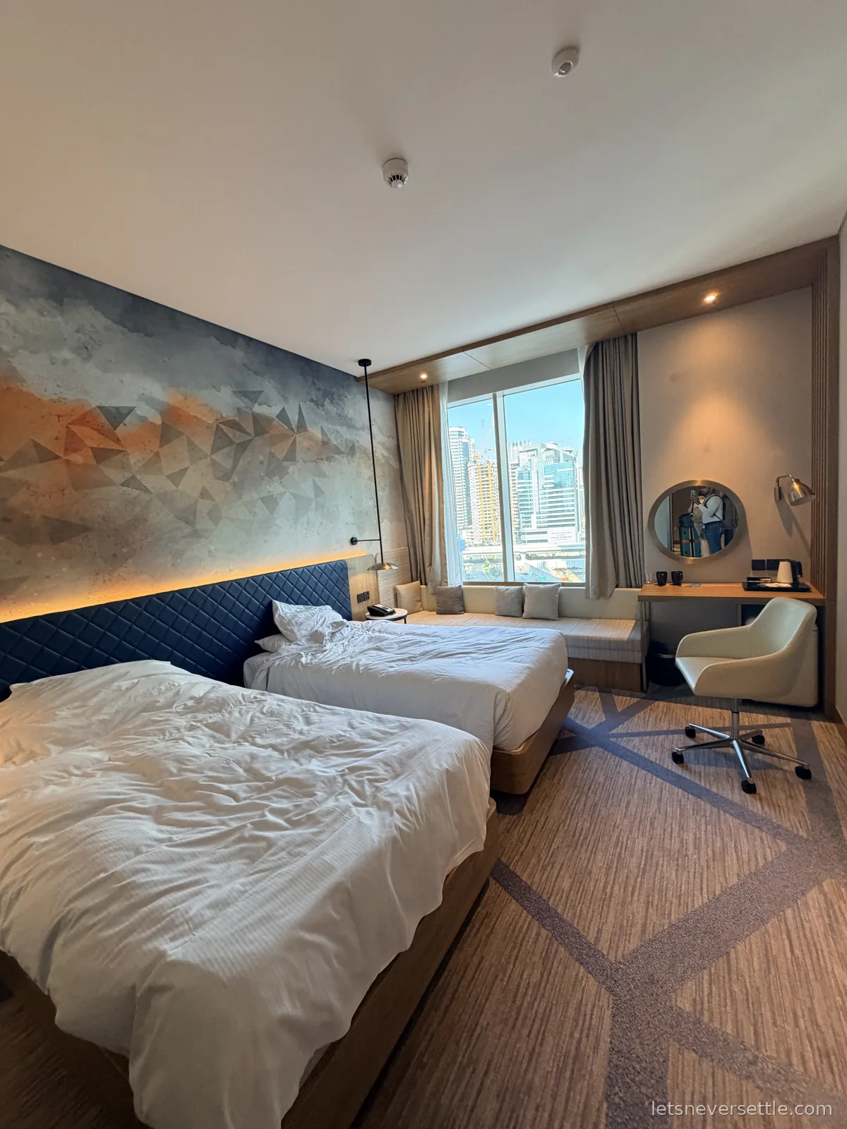 A Business Bay hotel room in Dubai, two beds, a patterned feature wall and a window seat looking out at the towers