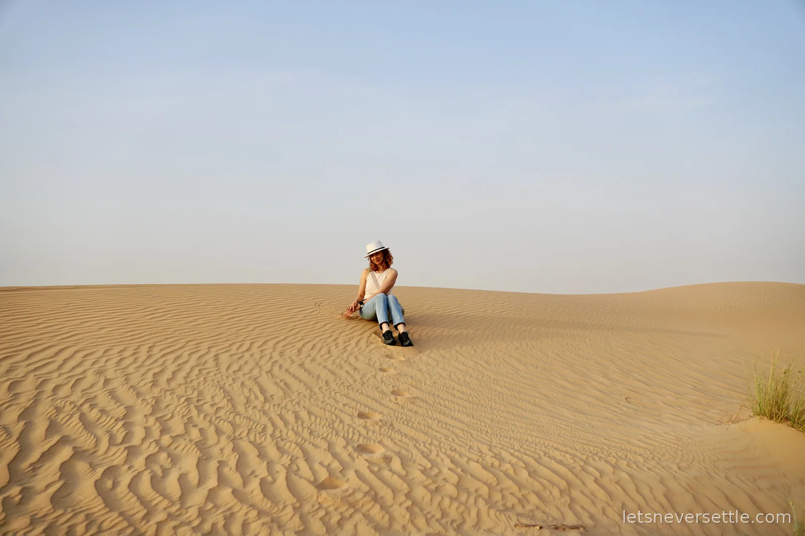 Inga sitting alone on a rippled sand dune in the Dubai desert, a line of footprints leading up to her