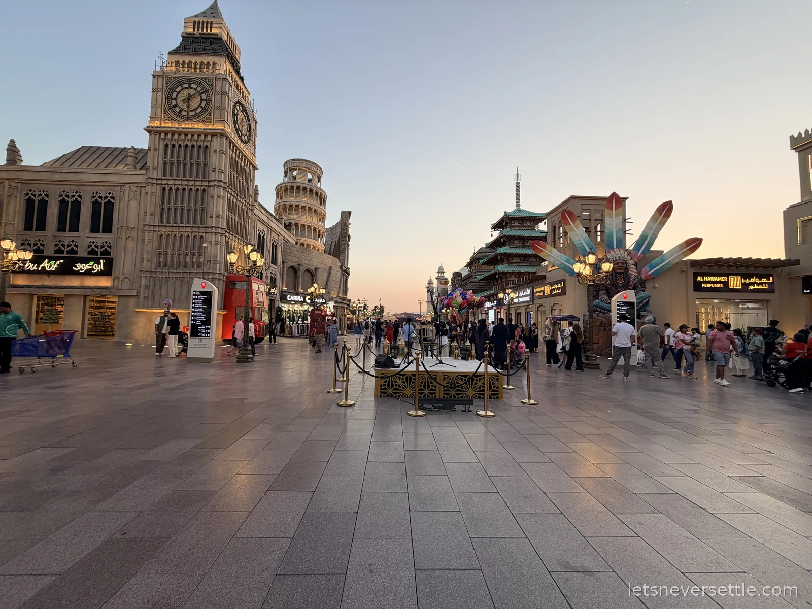 The main boulevard at Global Village in Dubai at dusk, with a replica Big Ben, a leaning tower and a Chinese pagoda along the same street
