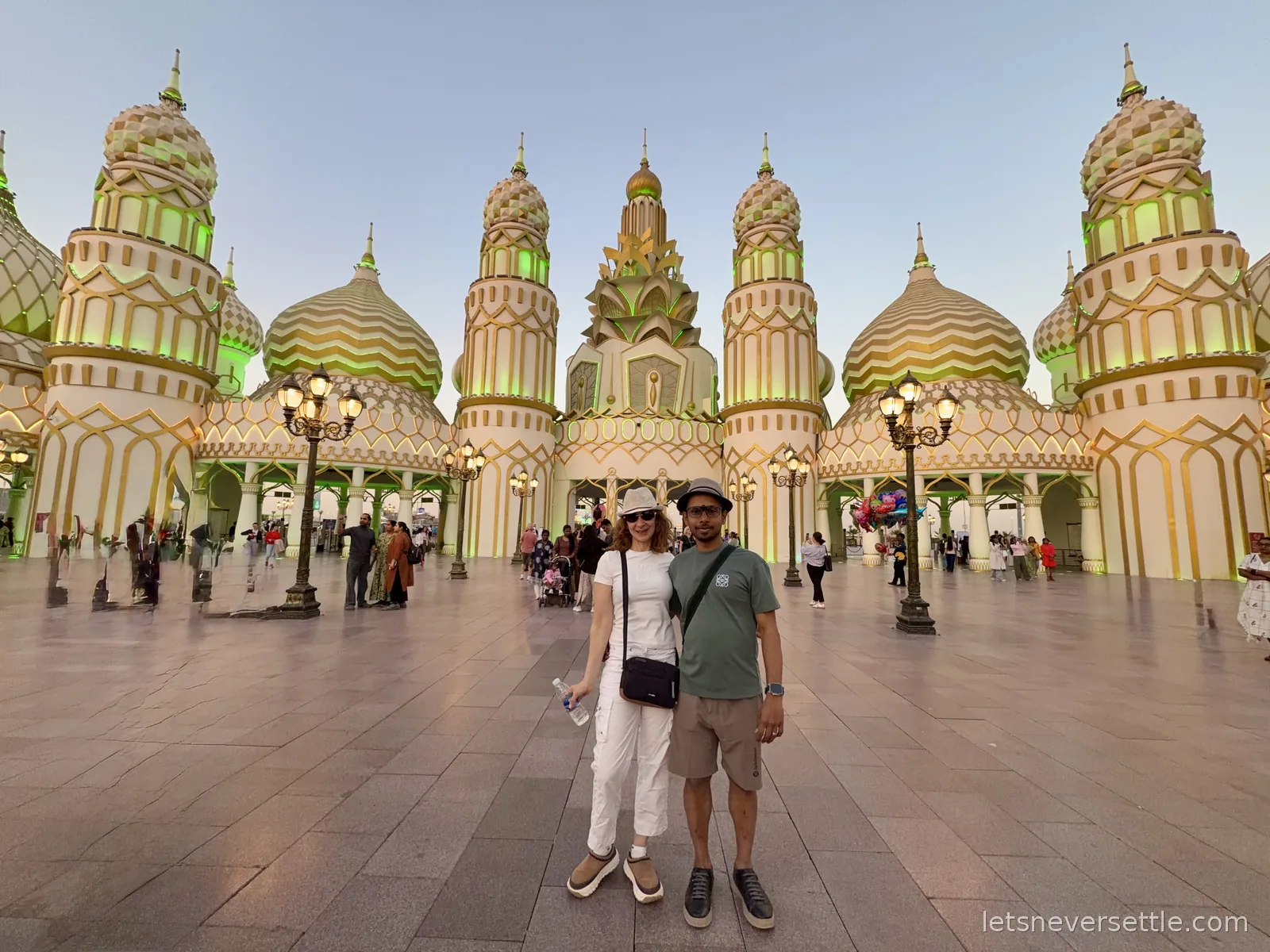 Inga and Dileep in front of the ornate domed and turreted Gate of the World at Global Village, Dubai, lit up at dusk
