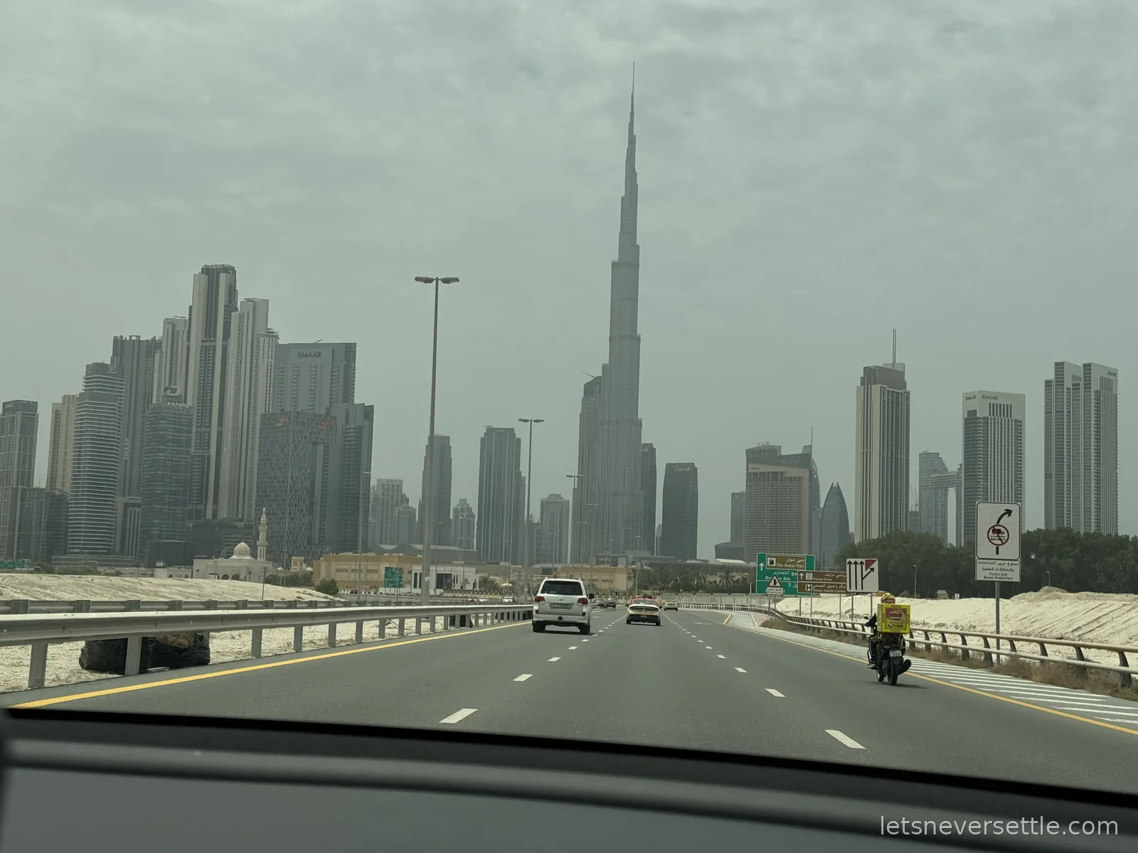 View through a car windscreen of the Downtown Dubai skyline on a hazy day, the Burj Khalifa rising above the other towers