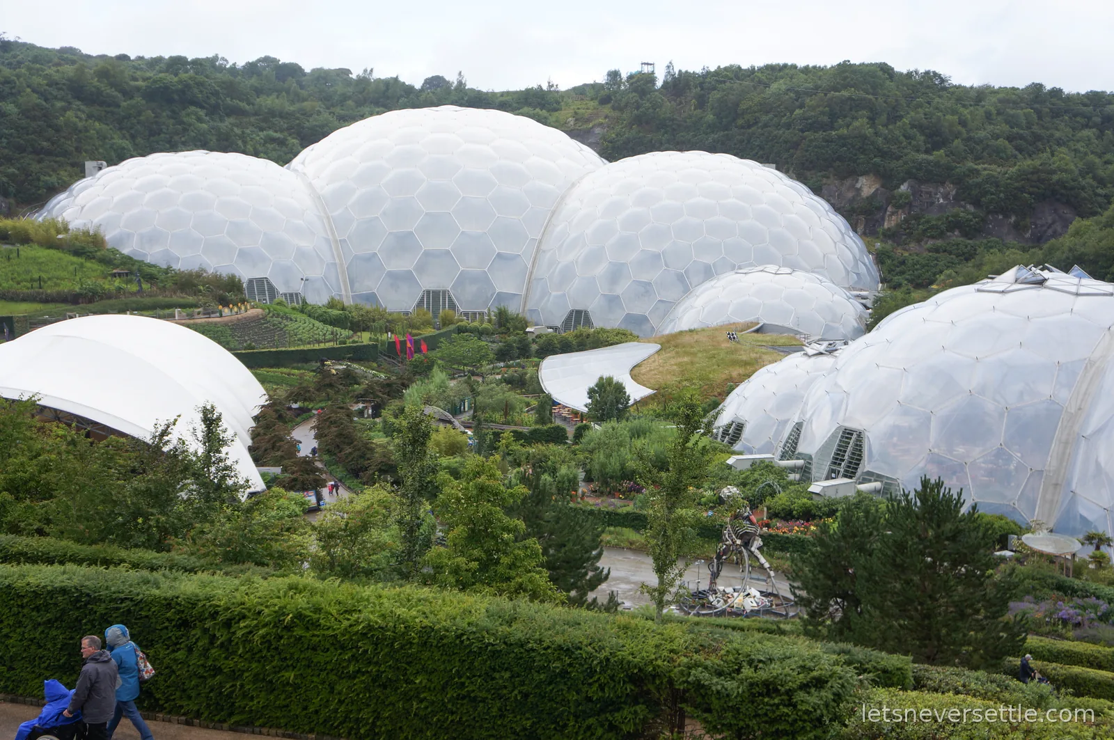 The hexagon-panelled biome domes of the Eden Project nestled in a green former clay pit with gardens and paths between them