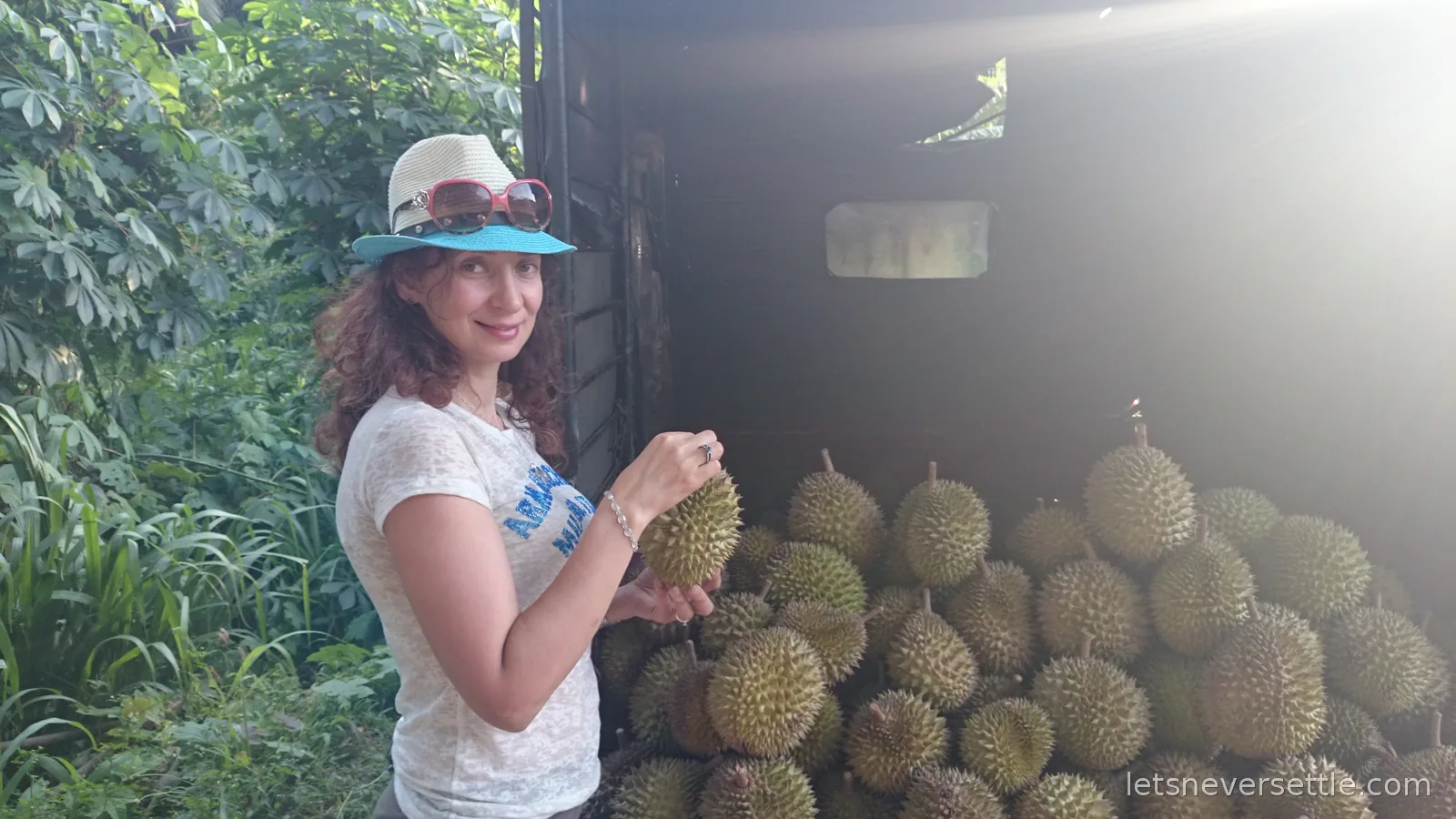 Inga in a sun hat holding a durian beside a truck loaded with spiky durian fruit