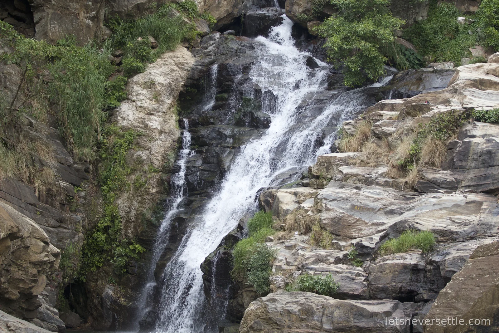 Ravana Falls cascading in white streams over dark rock ledges framed by green jungle