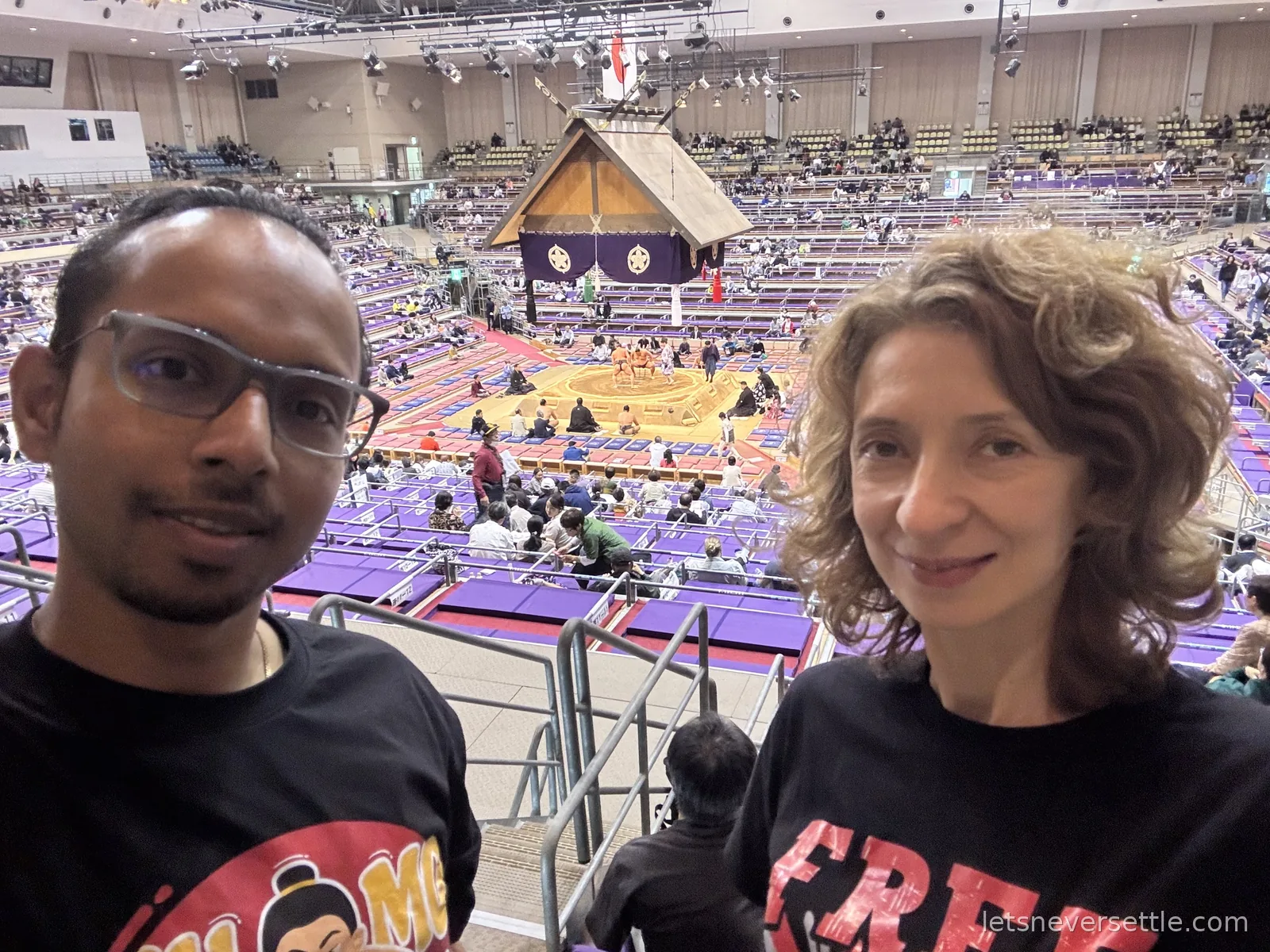 Inga and Dileep taking a selfie in the upper seats of the sumo arena with the roofed ring and purple seating below