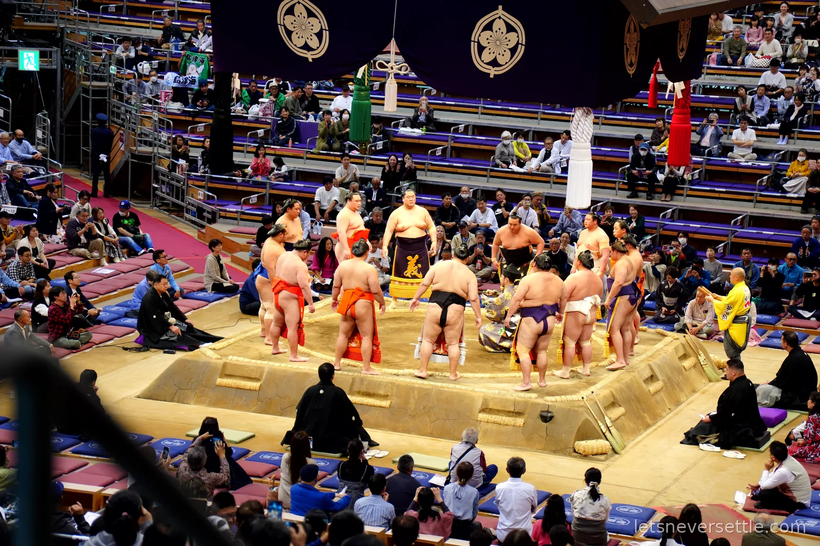 Sumo wrestlers in colourful ceremonial aprons standing in a circle around the raised clay ring during the ring-entering ceremony