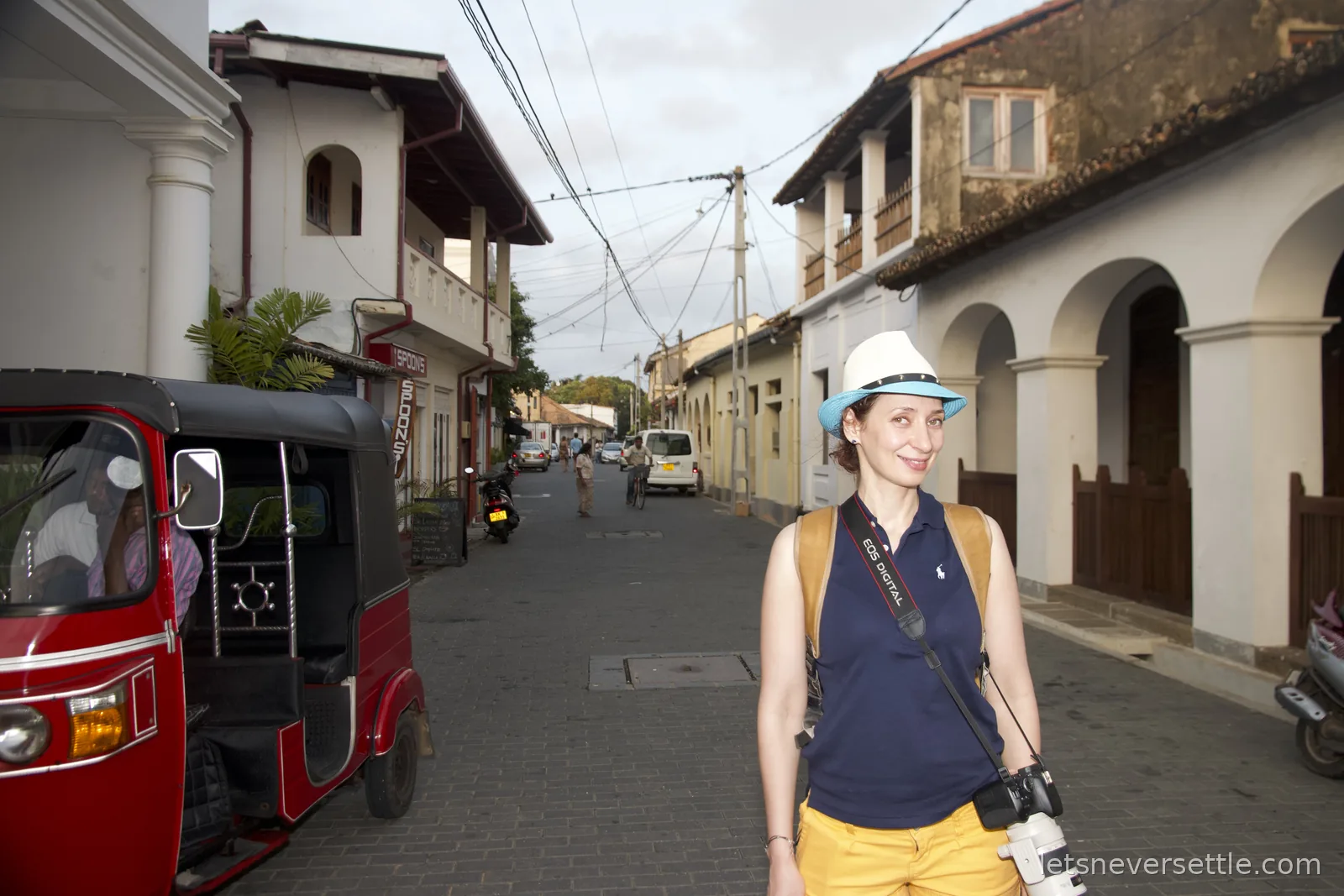 Inga in a straw hat on a street of old colonial buildings in Galle Fort, a red tuk-tuk parked to one side