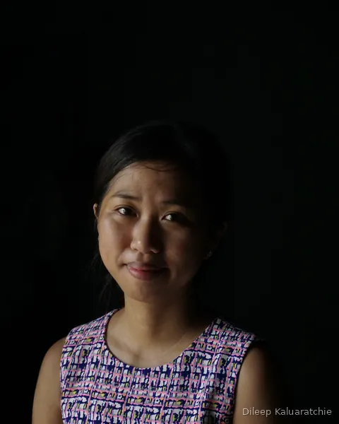 A young woman in a patterned sleeveless top, lit against a black background in Hoi An