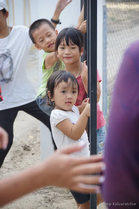 Children crowding around a fence post, one small girl looking straight down the lens