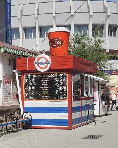 A red street coffee kiosk in Almaty with a giant takeaway cup on the roof and a chalkboard menu in Russian