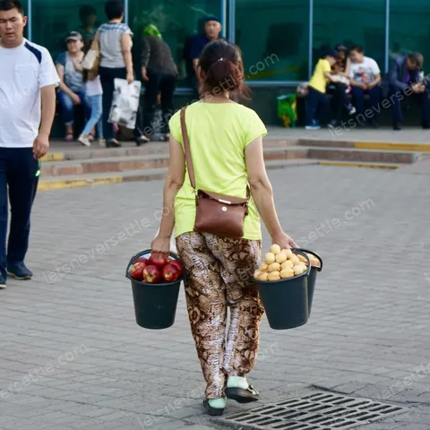 A woman carrying two full buckets of fruit away from the market