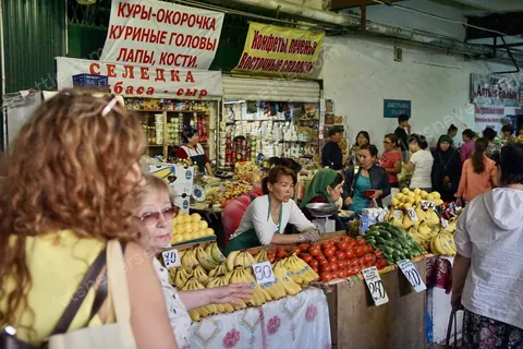 A fruit and vegetable stall in Almaty's Green Bazaar, bananas and tomatoes stacked under hand-lettered Russian signs
