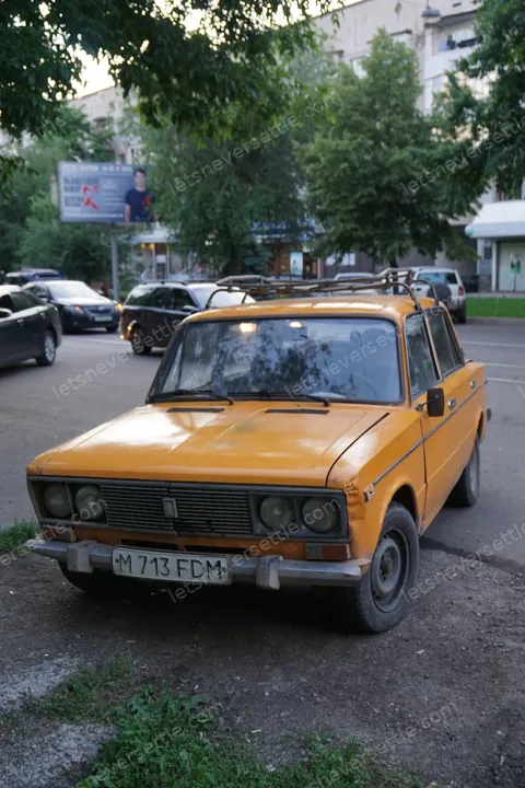 An orange Lada parked under the trees on an Almaty street
