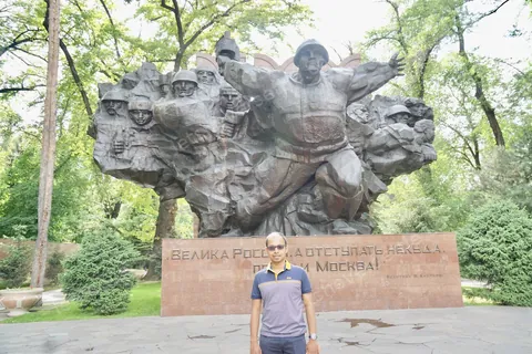 Dileep standing in front of the war memorial in Panfilov Park, Almaty, huge cast figures rising behind him