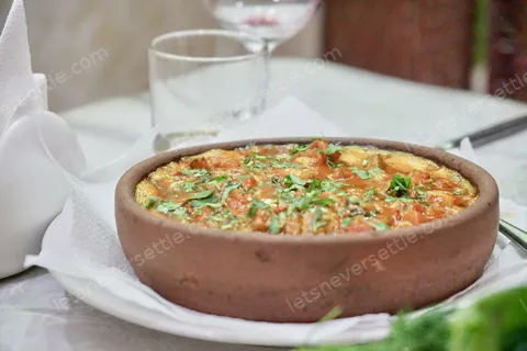 A clay bowl of soup scattered with fresh herbs on a white tablecloth