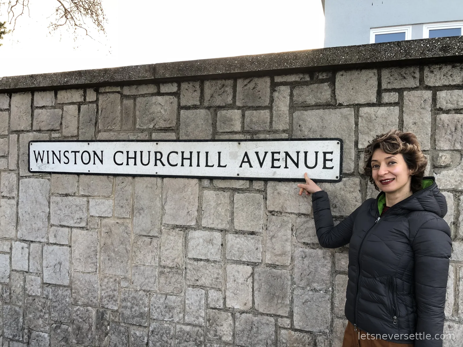 Inga pointing at a Winston Churchill Avenue street sign mounted on a stone wall in Gibraltar