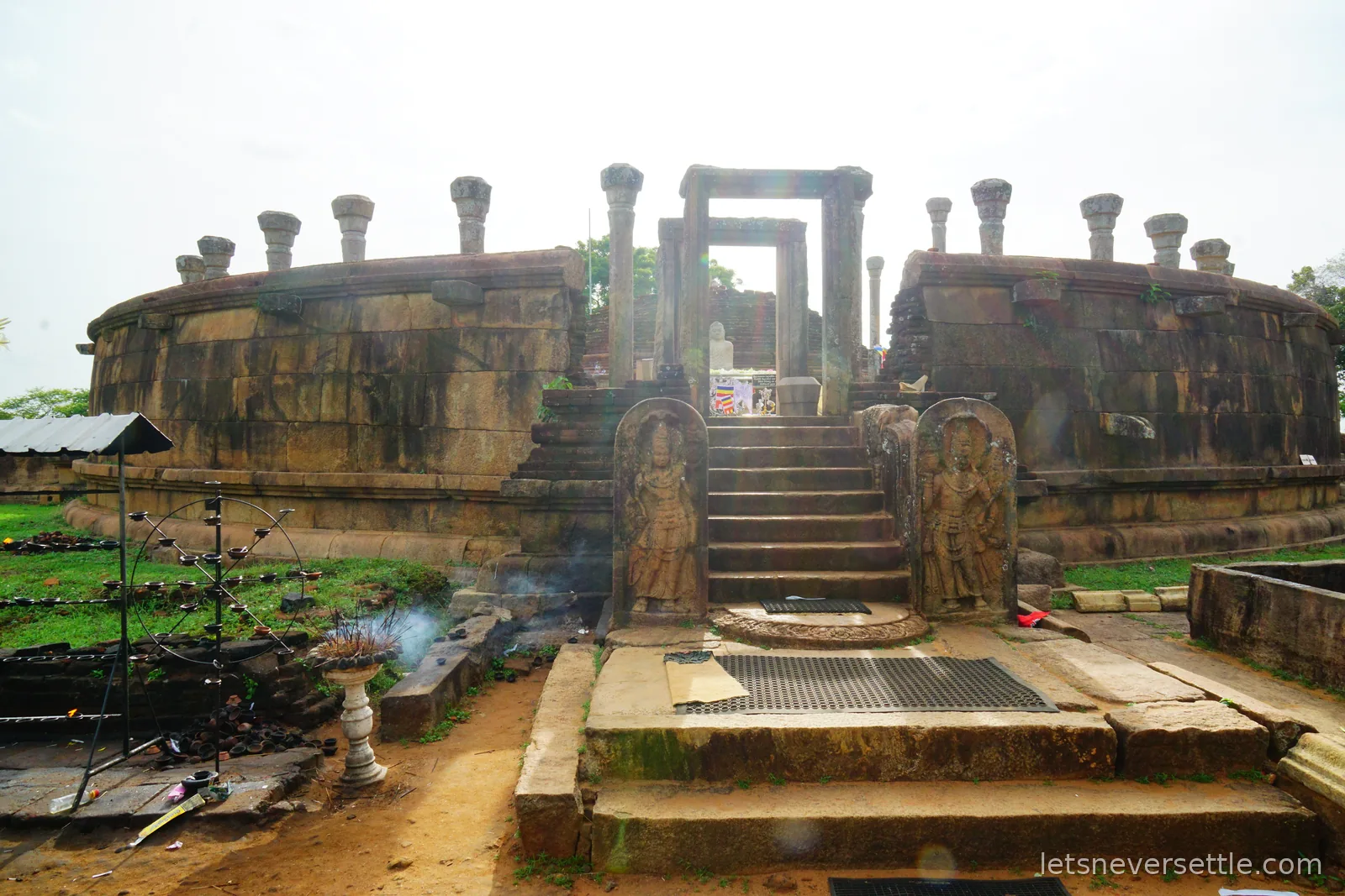 The stepped entrance to the circular stone vatadage at Girihandu Seya, flanked by two carved guardstone slabs, with an oil lamp stand smoking in the foreground