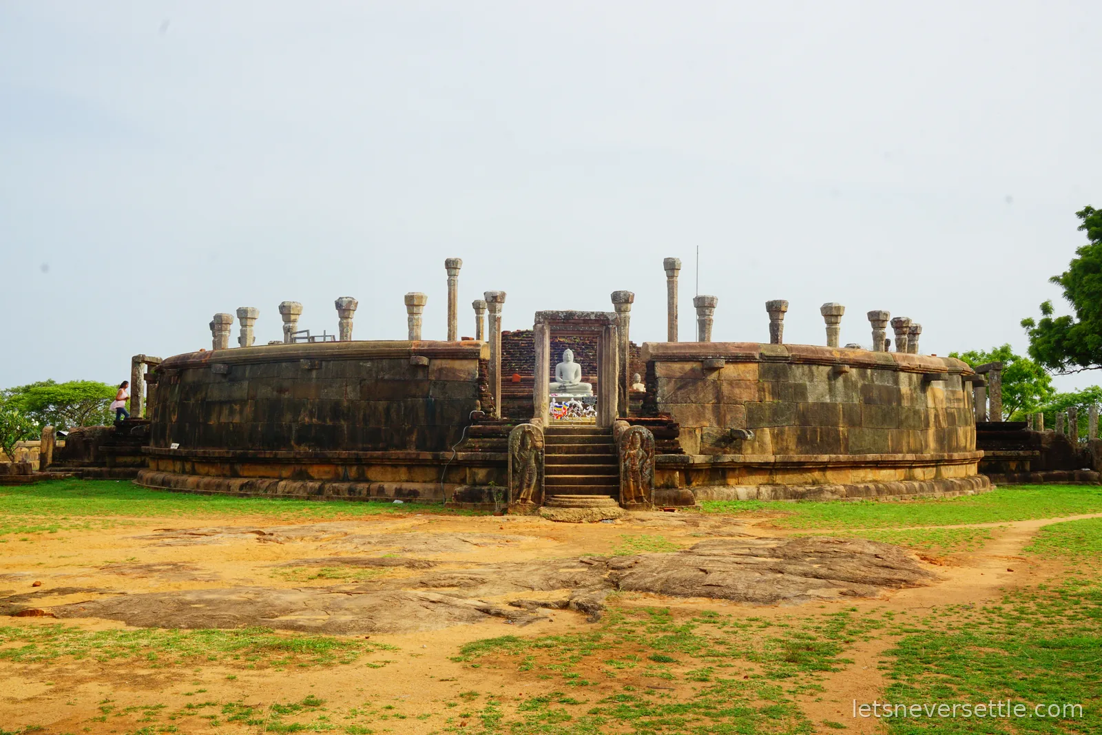 Wide view of the circular stone vatadage at Girihandu Seya, its outer wall ringed with short stone pillars and bare rock in the foreground