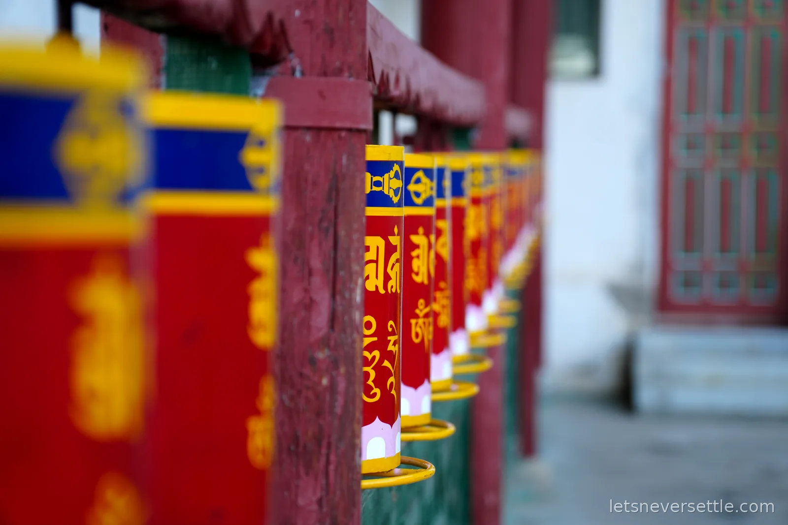 A long row of red, blue and gold prayer wheels mounted along a crimson rail at the Aryabal meditation temple in Gorkhi-Terelj National Park