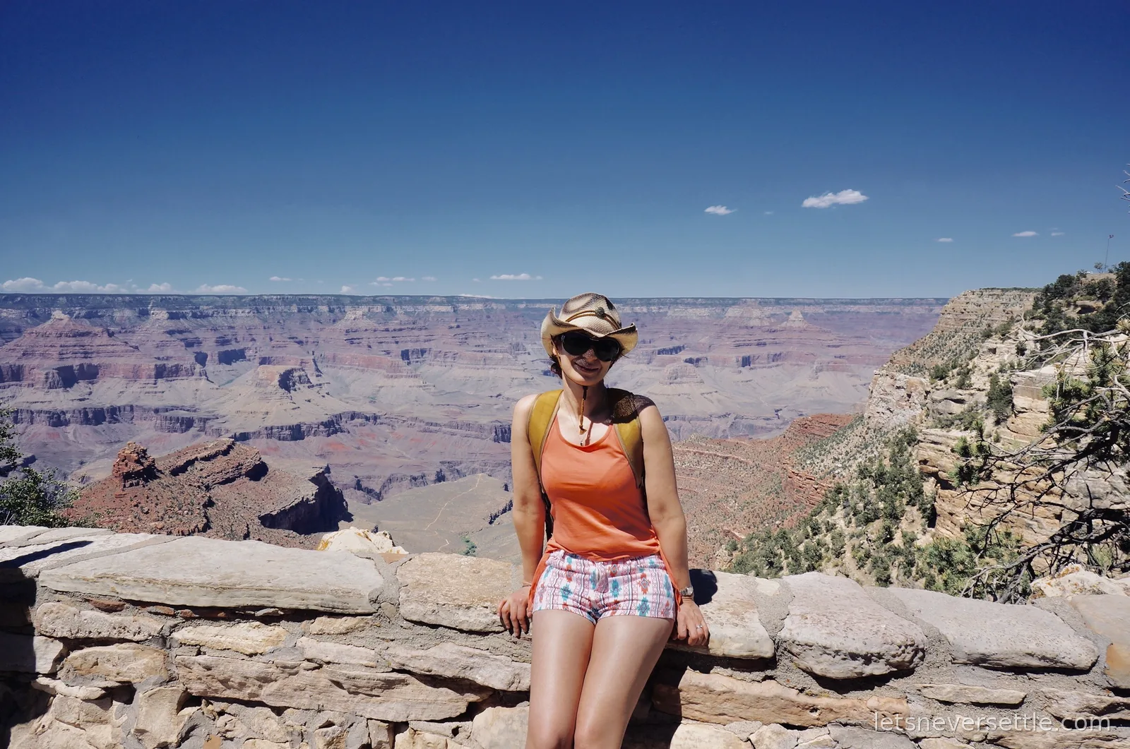 Inga in a straw cowboy hat sitting on the stone rim wall with the canyon dropping away behind her