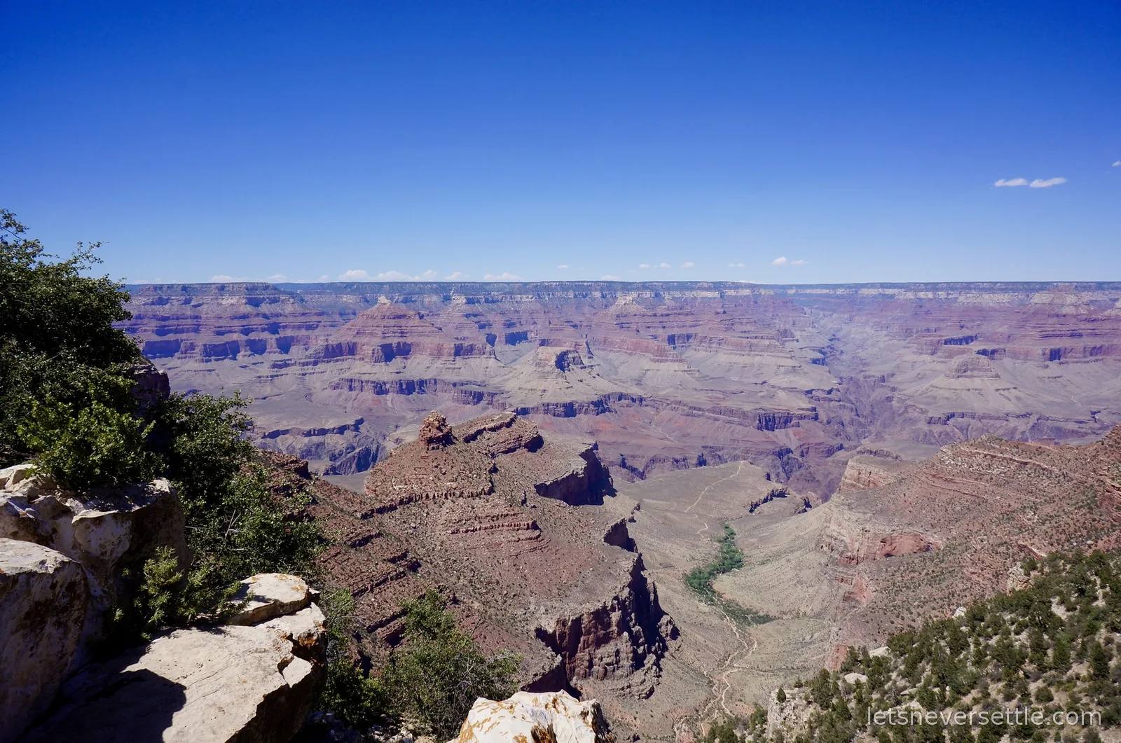Layered red and cream rock buttes of the Grand Canyon stretching to the horizon under a hazy blue sky