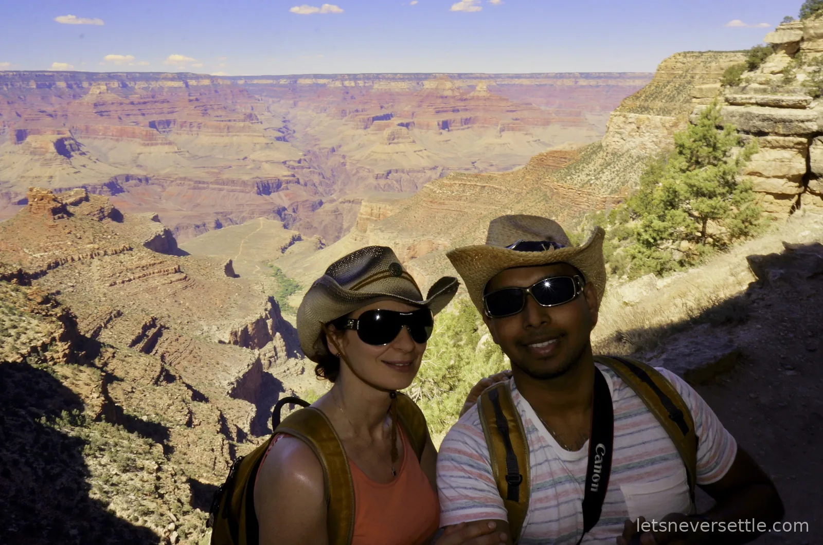Selfie of Inga and Dileep in straw hats on a dusty trail below the canyon rim