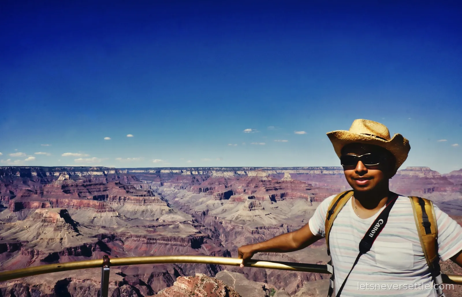 Dileep leaning on a viewpoint railing with canyon walls behind under a deep blue sky