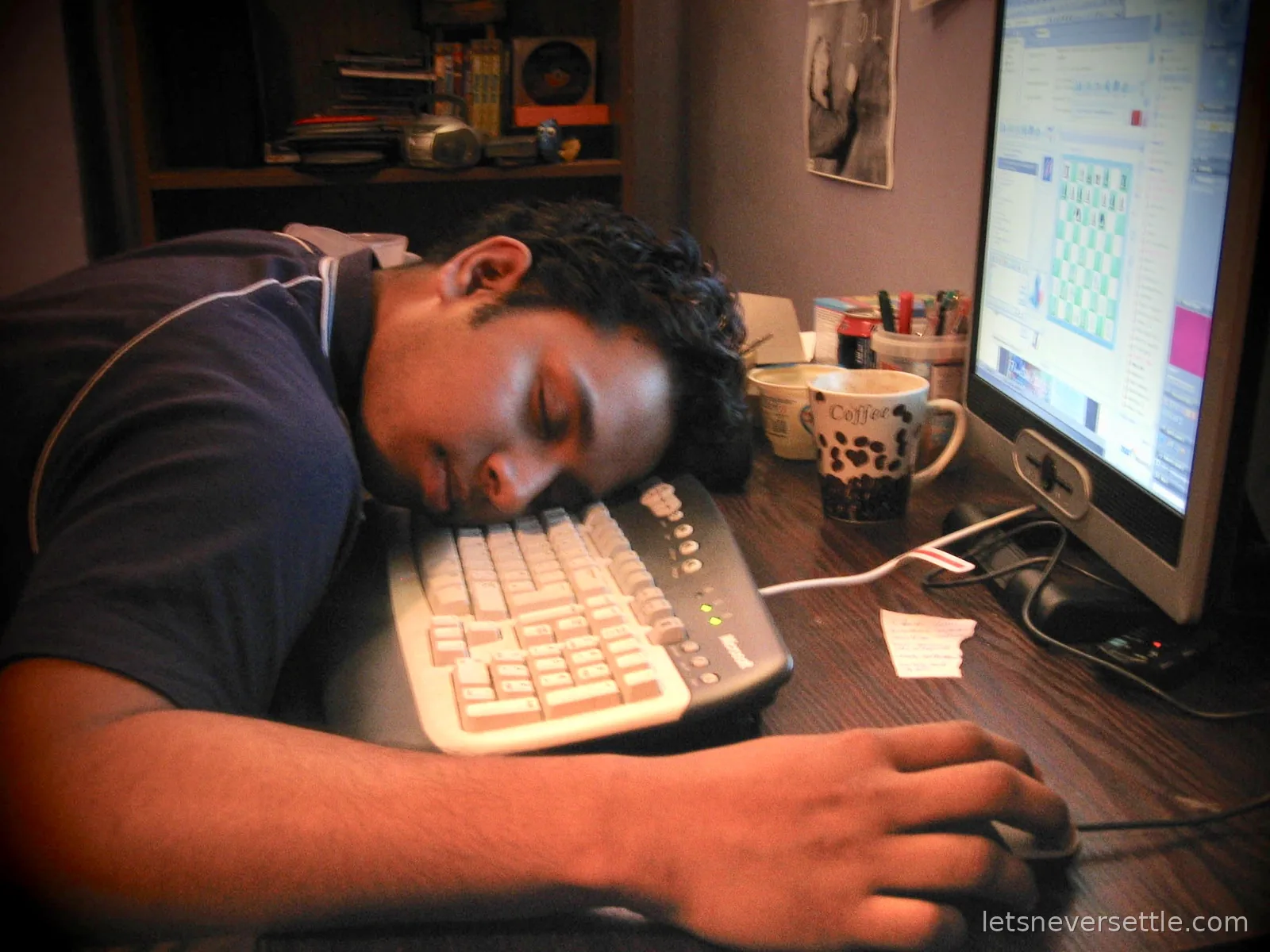 Dileep asleep face down on a keyboard at a desk, one hand still on the mouse, two coffee mugs beside him and a monitor showing an unfinished game of chess