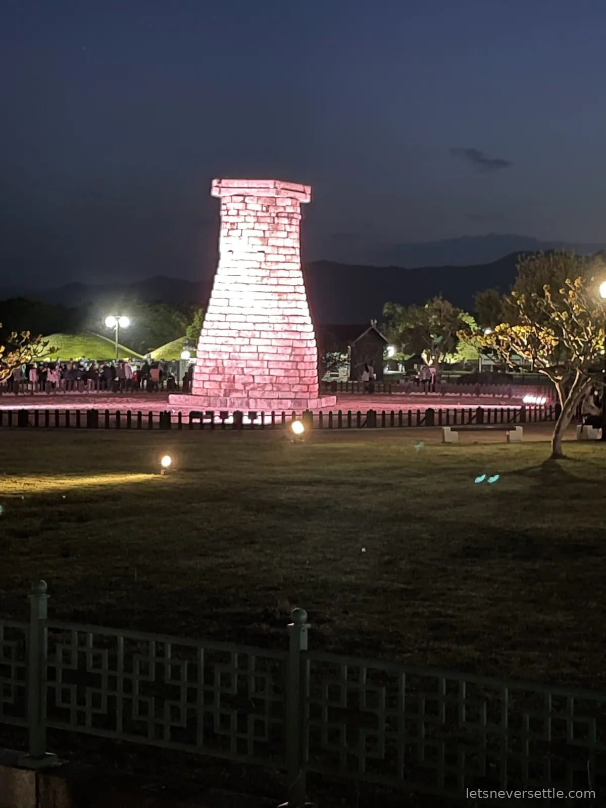 Cheomseongdae, the ancient bottle-shaped stone observatory in Gyeongju, illuminated pink against a deep blue dusk sky
