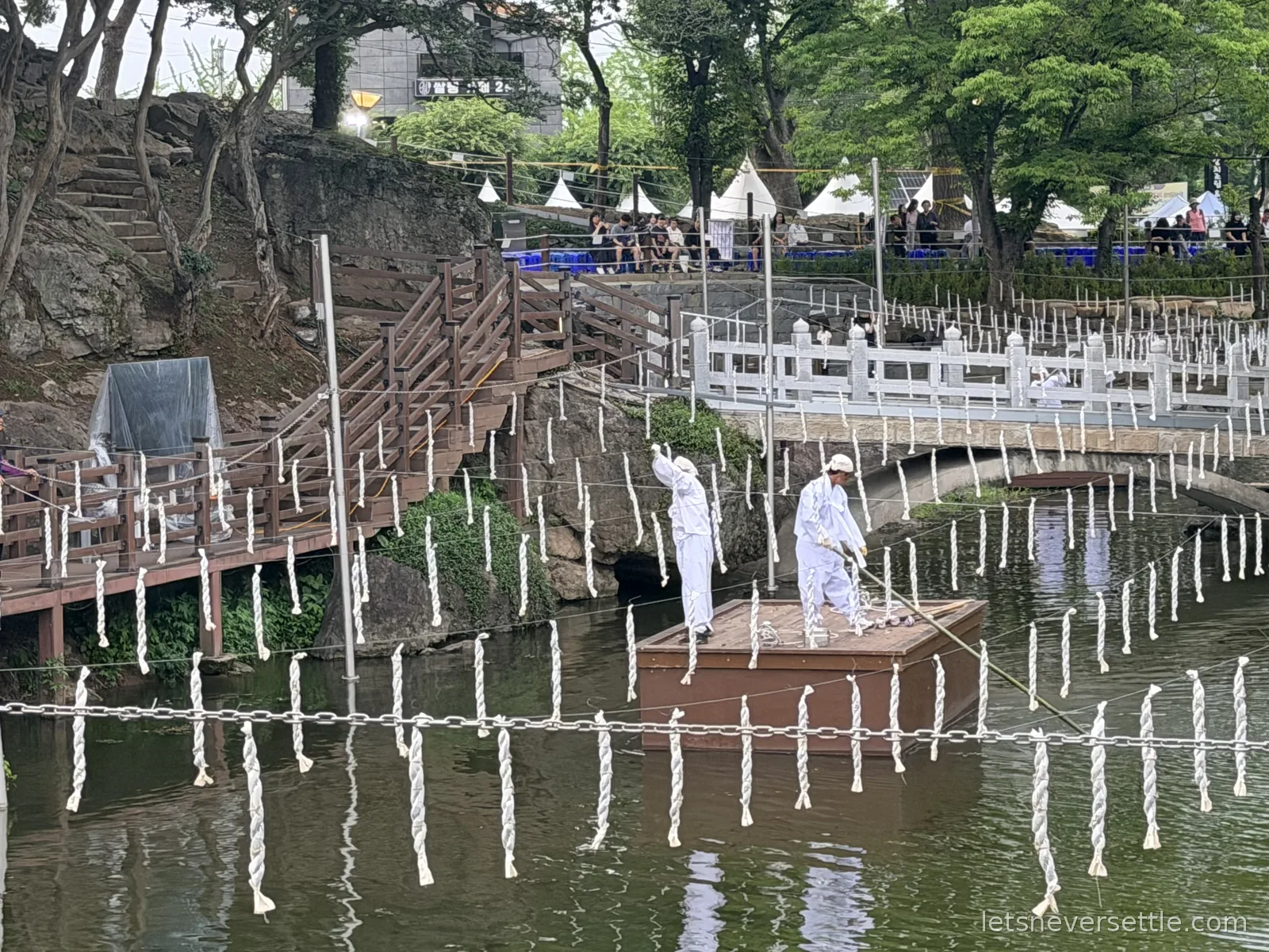 Hundreds of white charcoal torches hanging from ropes strung across the pond at Mujinjeong while two men in white work from a wooden raft