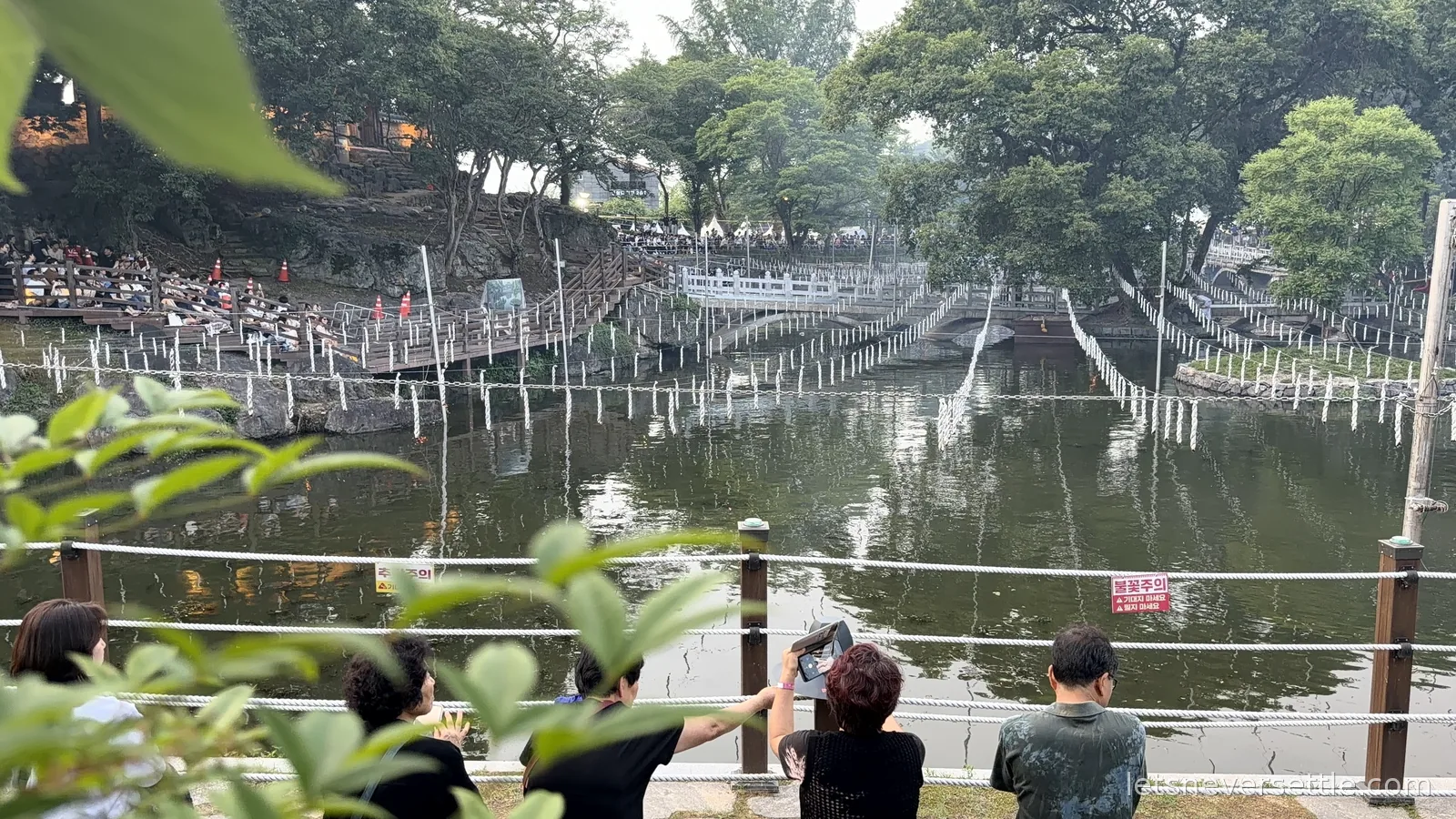 Wide view across the Mujinjeong pond in Haman with rows of unlit charcoal torches on ropes and spectators lining the railings