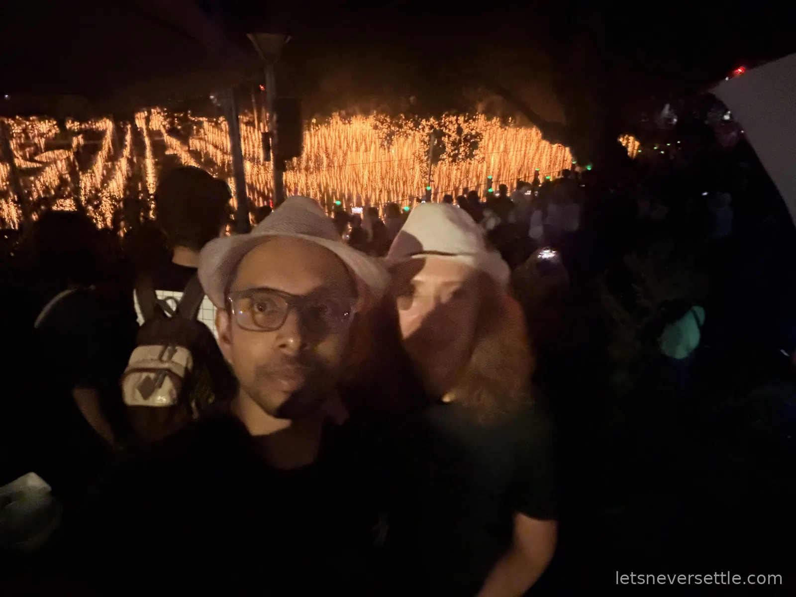 Night selfie of Inga and Dileep in hats with the burning nakhwanori ropes and a crowd of spectators behind them
