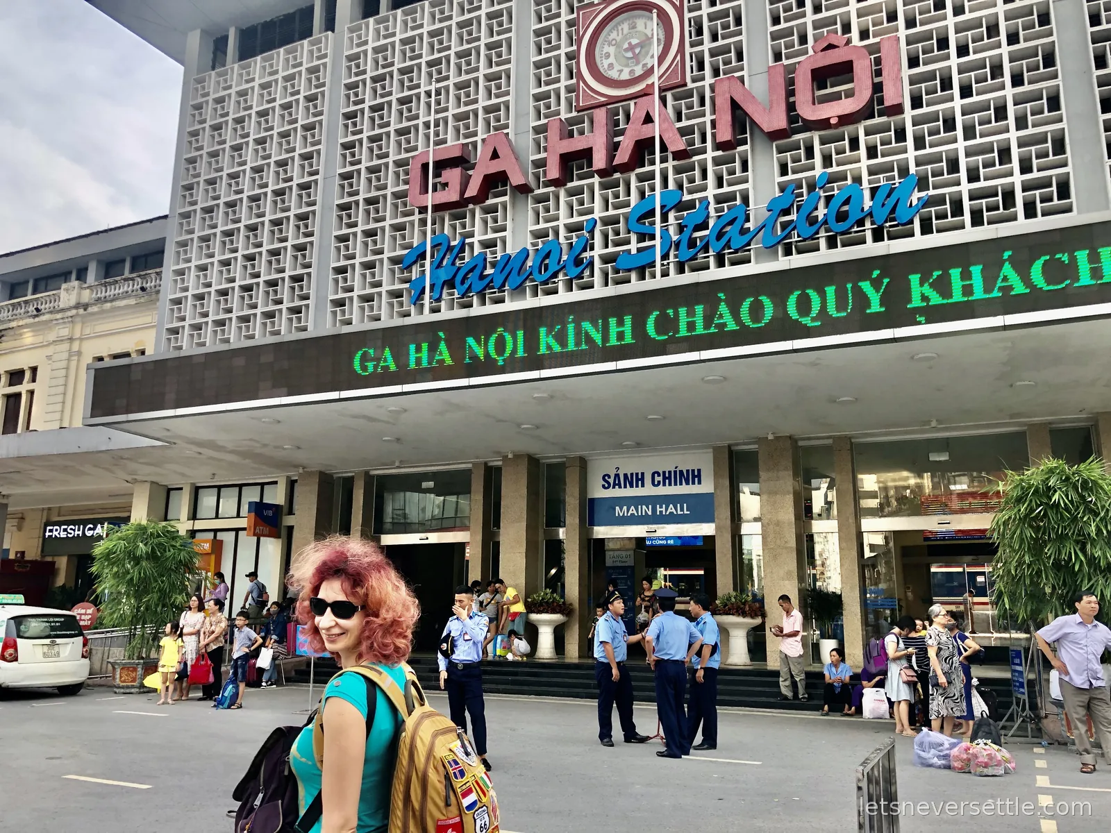 Inga with a patch-covered backpack outside Ga Ha Noi, the Hanoi railway station, its lattice facade and clock above the main hall entrance