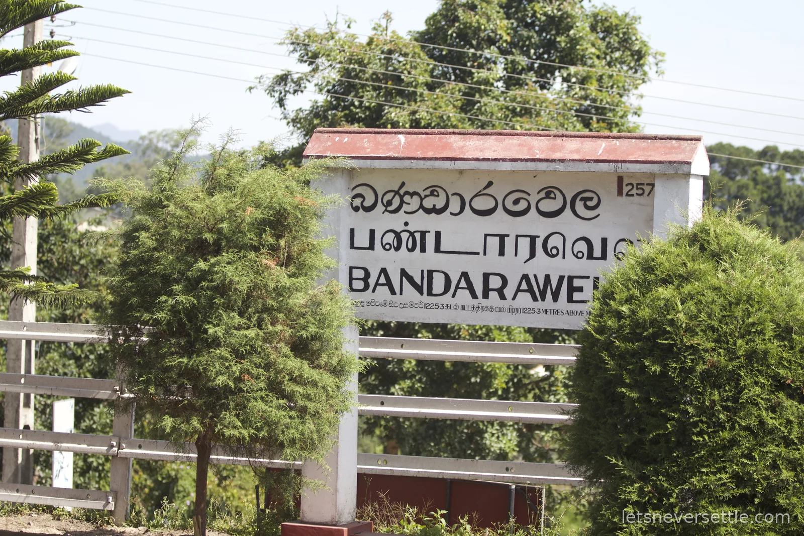Bandarawela station name board in Sinhala, Tamil and English behind a white trackside fence