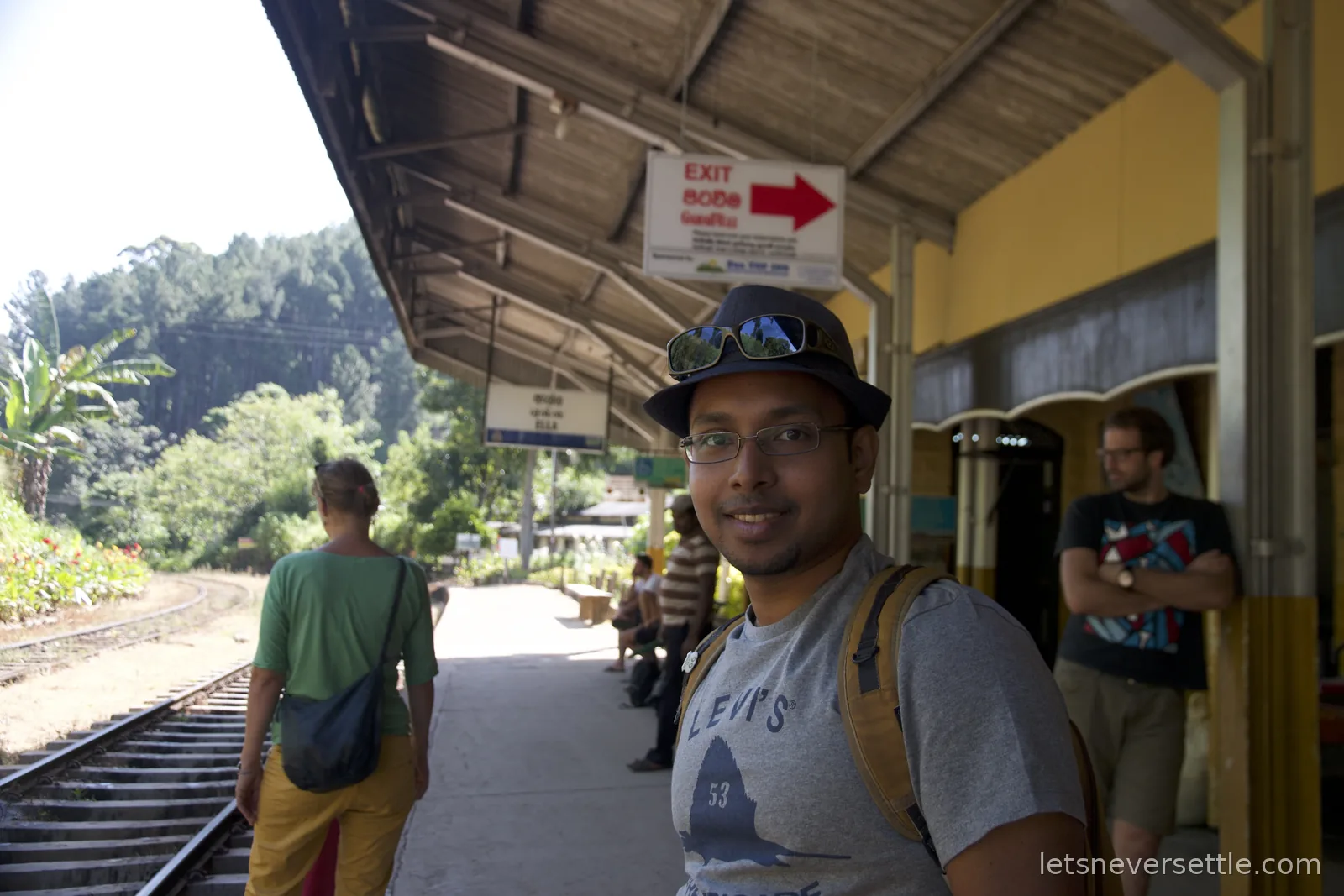 Dileep in a hat with a rucksack on the platform at Ella station, other travellers waiting in the shade of the canopy