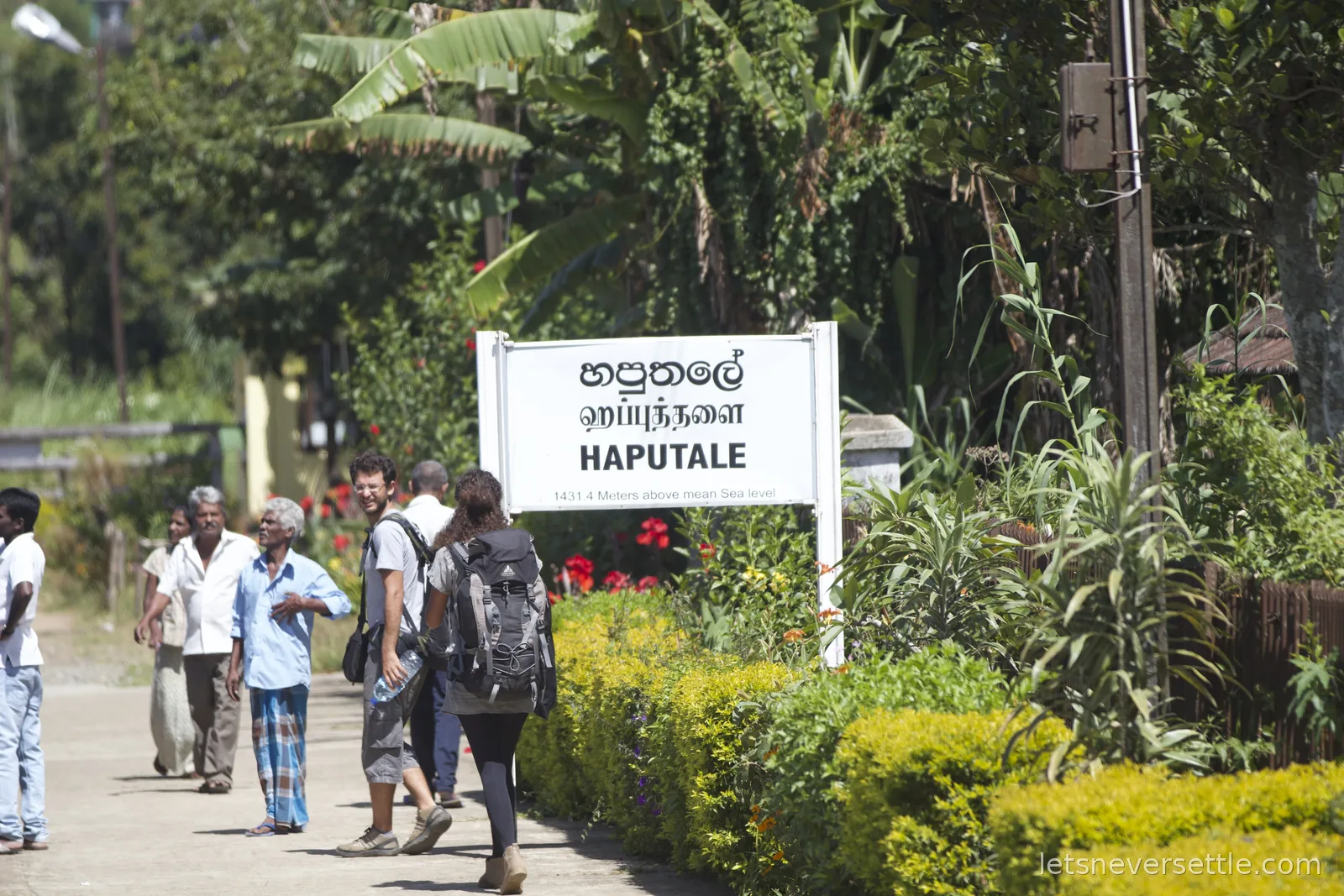 Haputale station sign in three languages noting 1431.4 metres above mean sea level, backpackers standing beside it