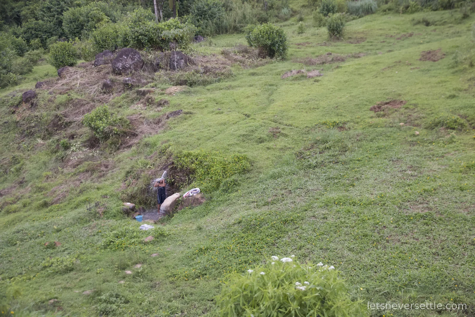 A man washing at a small spring on a green hillside, seen from the passing train