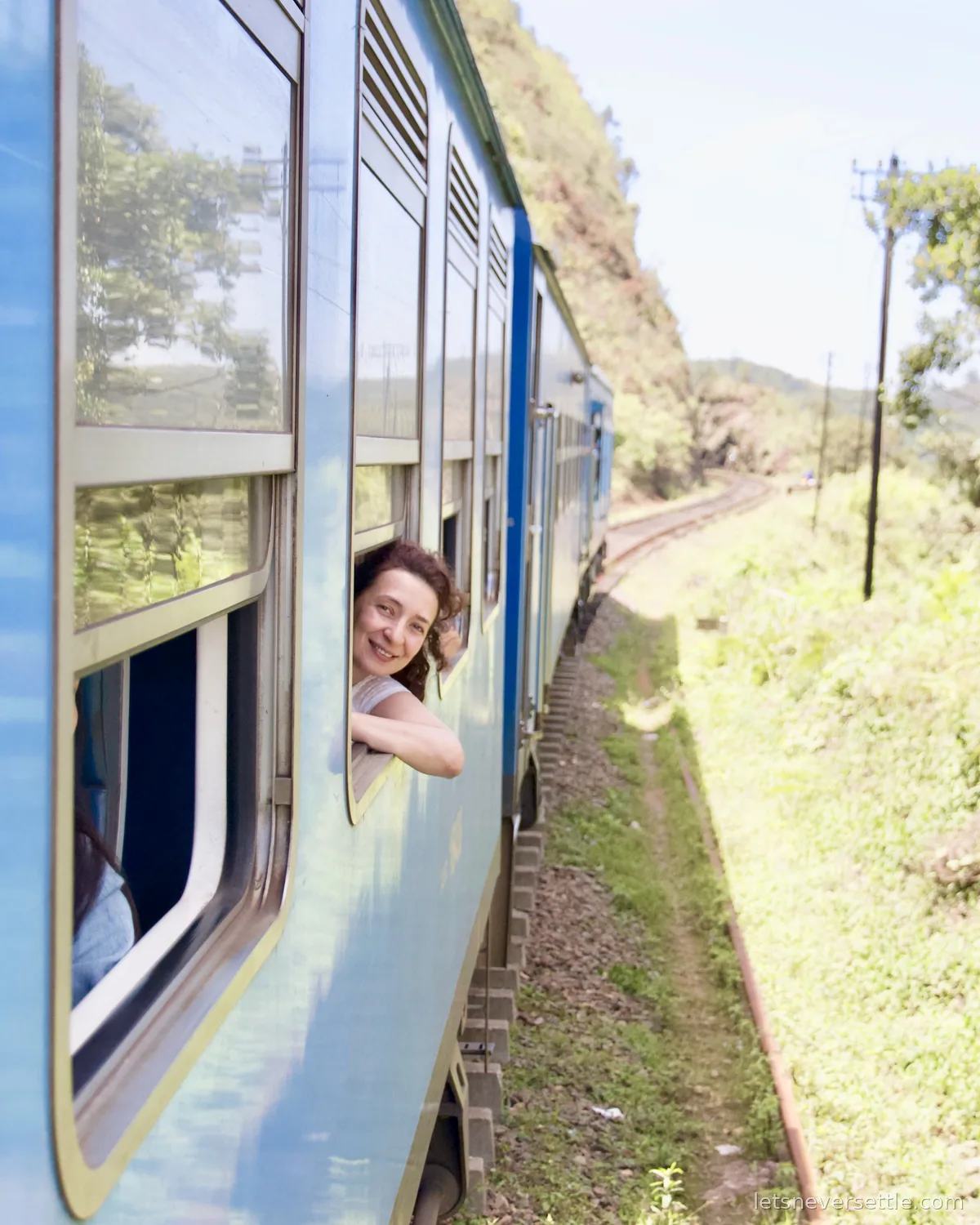 Inga leaning out of a blue carriage window and smiling back down the line of the train