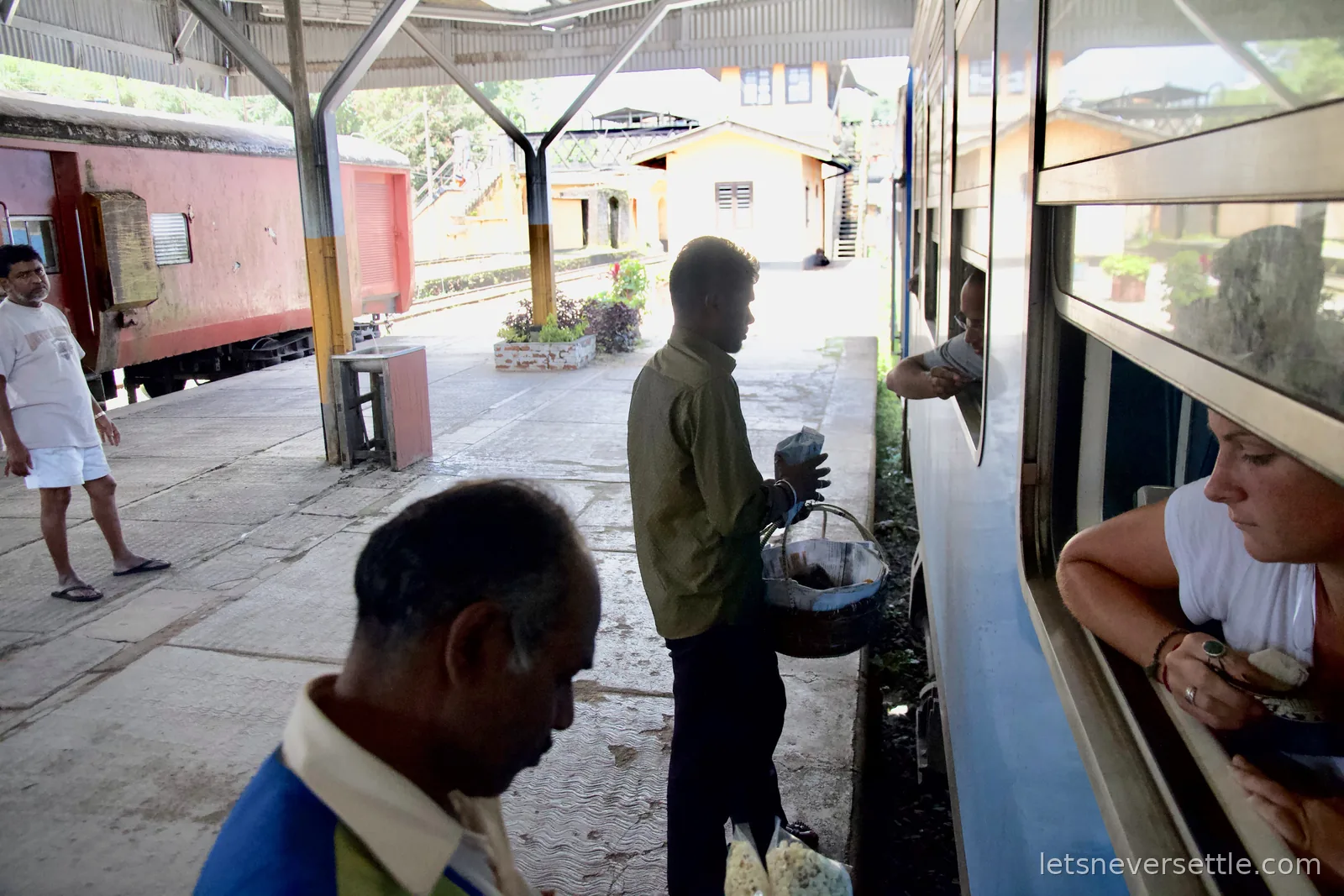 A hawker with a basket selling snacks to passengers through the open train window at a platform