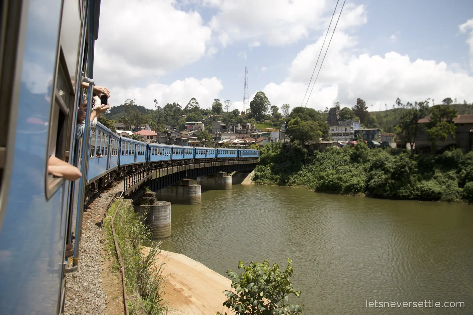 View from the carriage window of the train curving over a river bridge, arms and phones out of the windows ahead