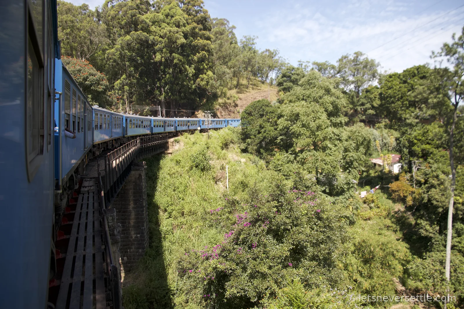 The line of blue carriages ahead crossing a narrow stone viaduct above a wooded valley