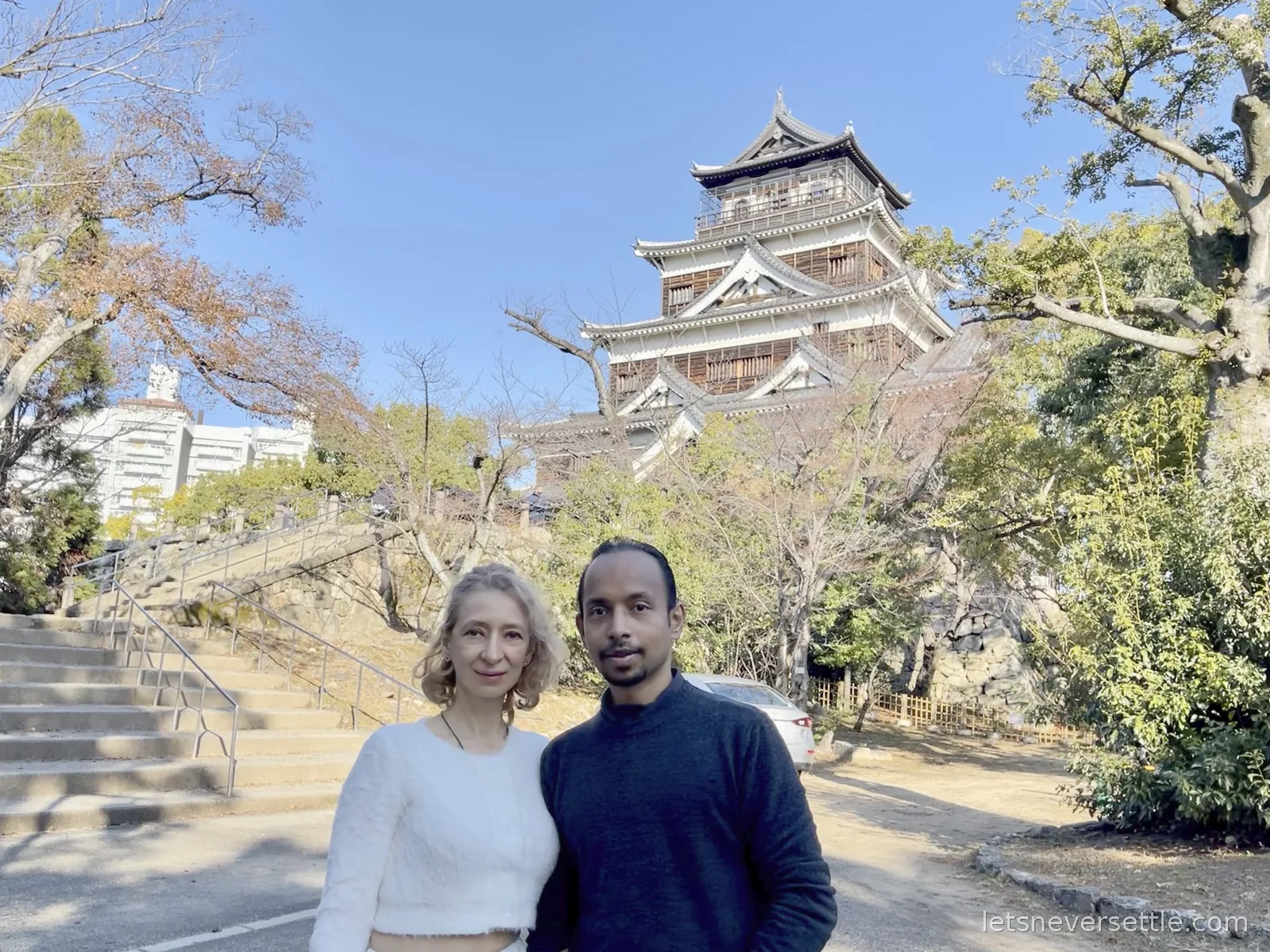 Inga and Dileep in front of Hiroshima Castle, its dark wooden keep rising above stone walls and bare December trees