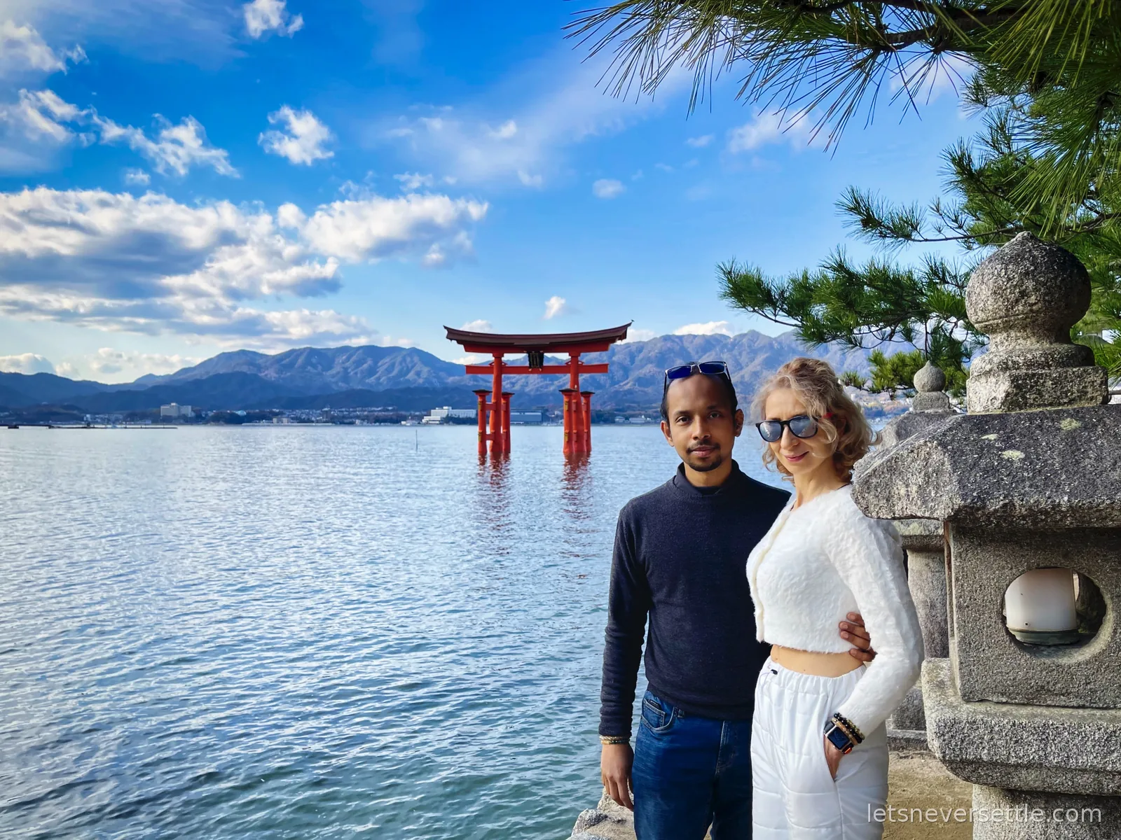 Inga and Dileep on the shore of Miyajima with the great orange torii gate standing in the sea behind them