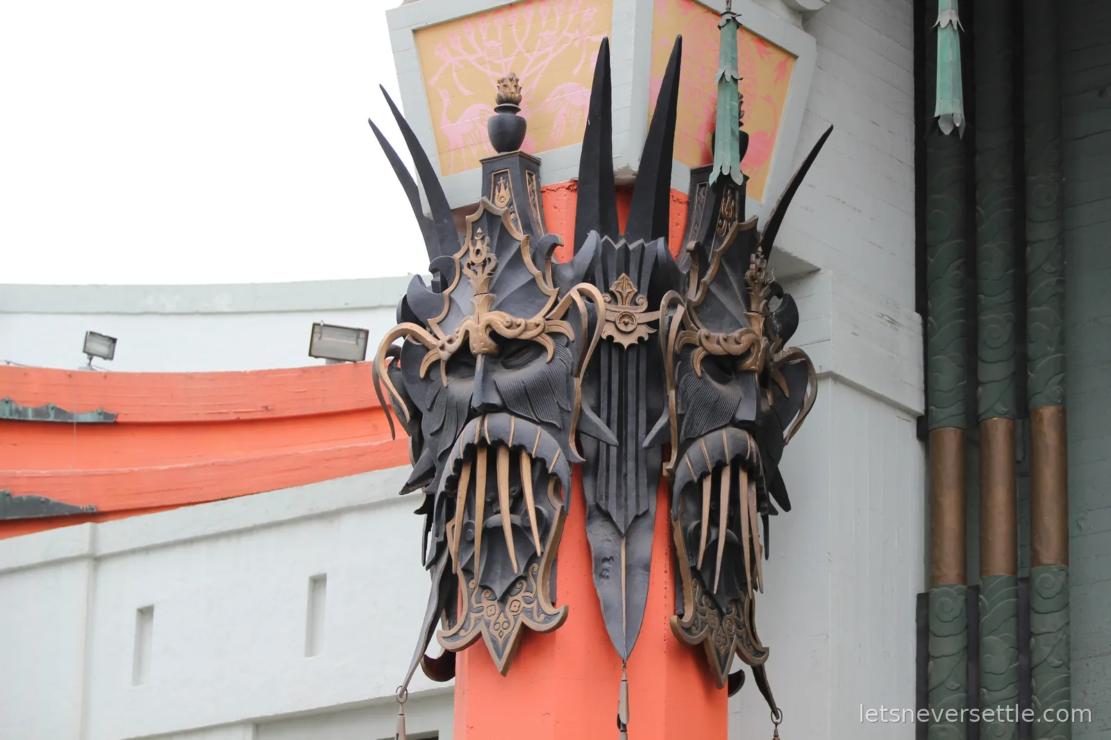 Black and bronze carved masks mounted on an orange column of the Chinese Theatre facade